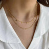Layered gold necklace with geometric charms on a woman wearing a white blouse