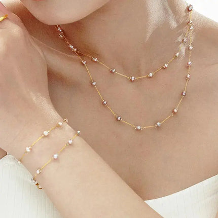 Woman wearing gold chain necklace and bracelet with small pearls, delicate jewellery style