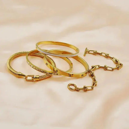 Gold stainless steel bangles and chain bracelet on pale fabric background