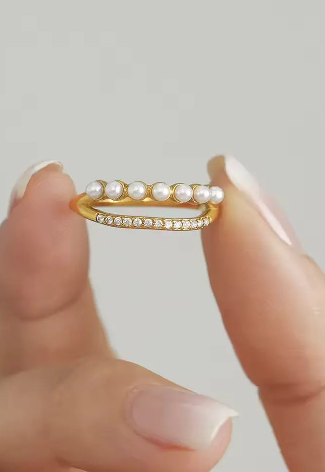 Gold ring with pearls held between two fingers against a neutral background