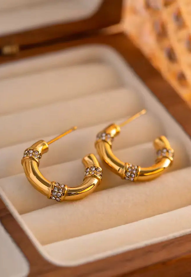Gold hoop earrings with embedded stones in a jewelry box.