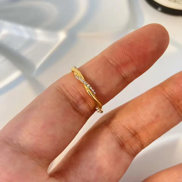 Gold ring with small diamonds on a finger against a neutral background
