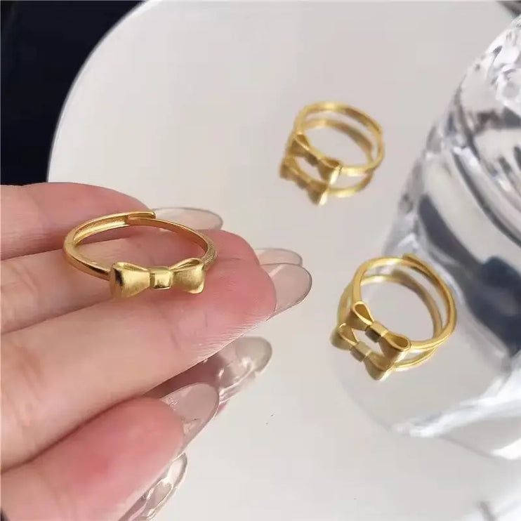 Gold bow-shaped ring held by a hand with additional rings on a white surface.
