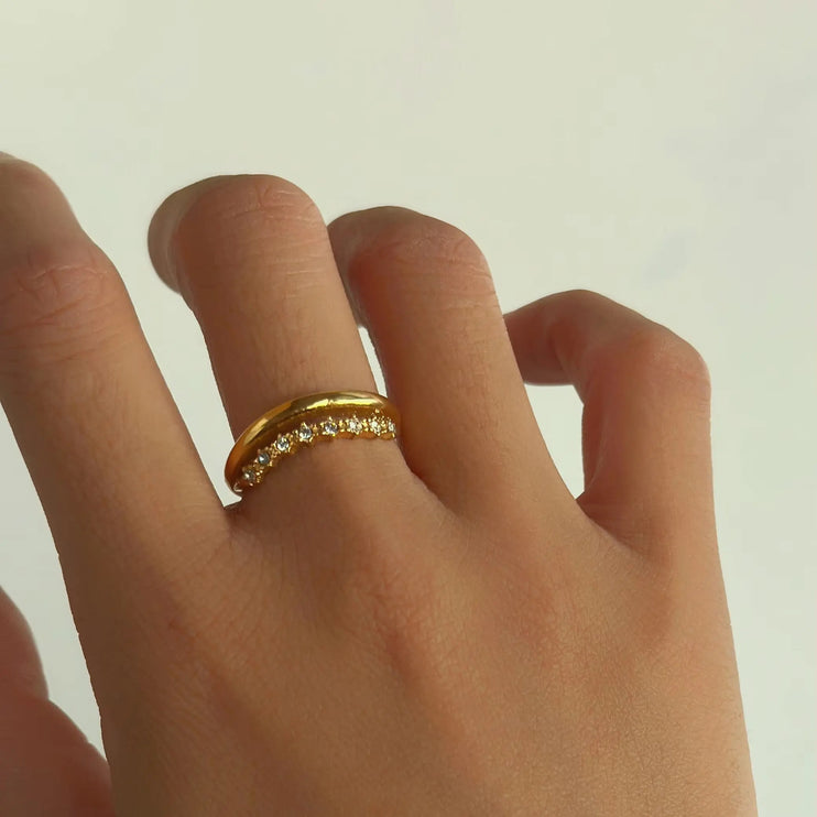 Gold ring with small diamonds on a person's finger against a plain background