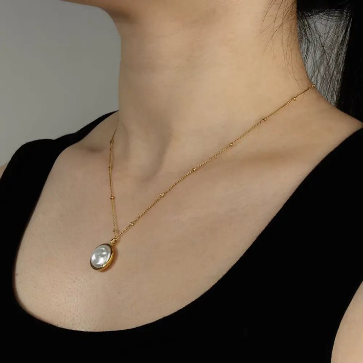 Gold necklace with a pendant on a person wearing a black top against a neutral background