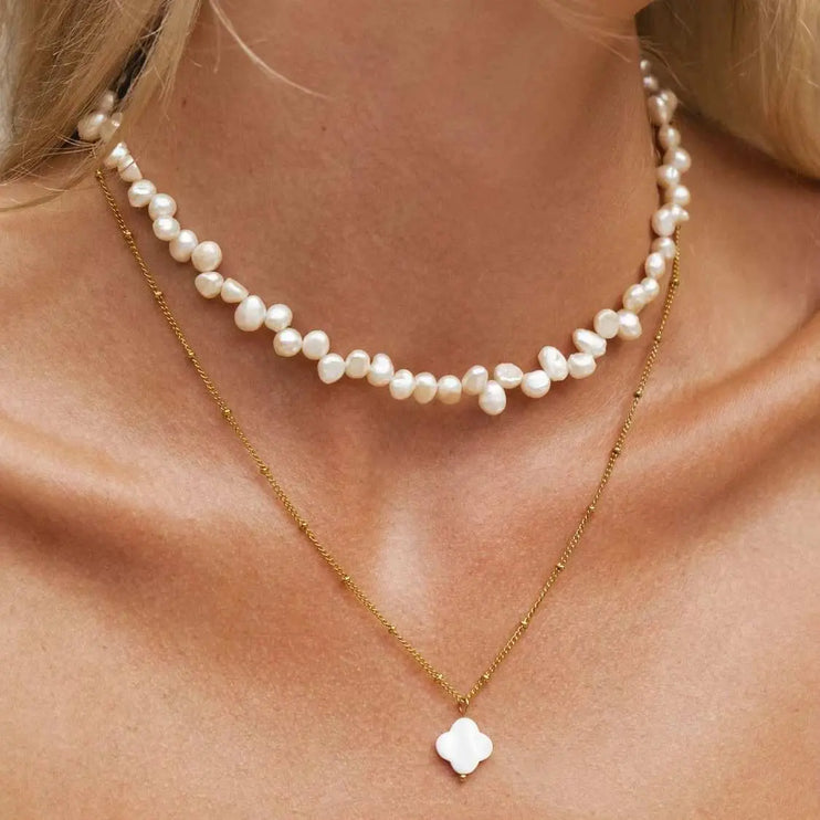 Pearl necklace and gold necklace with a clover pendant on a person's neck.