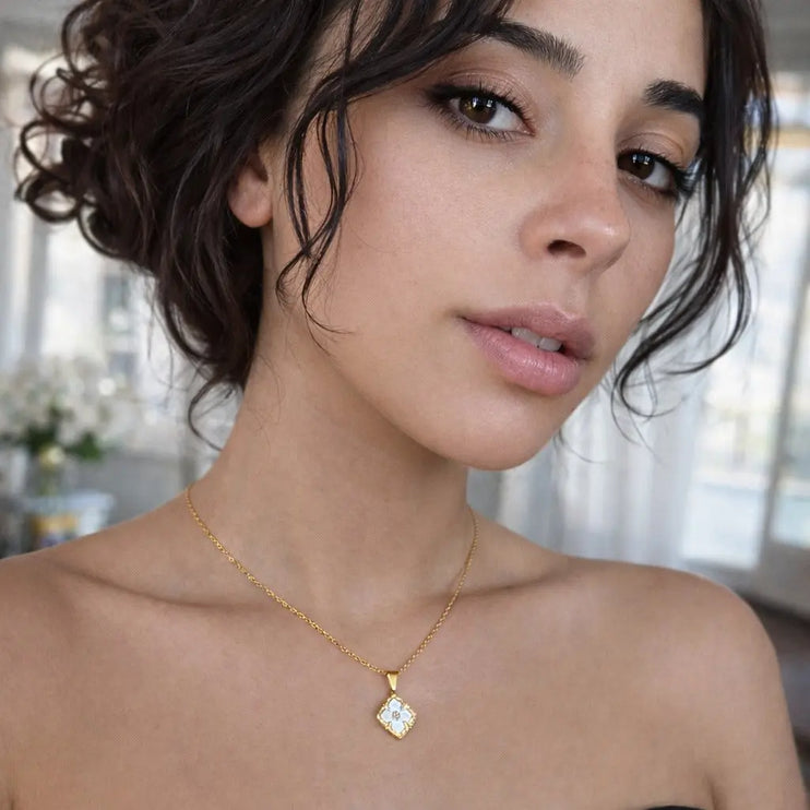 Woman wearing a gold necklace with a clear pendant in an indoor setting