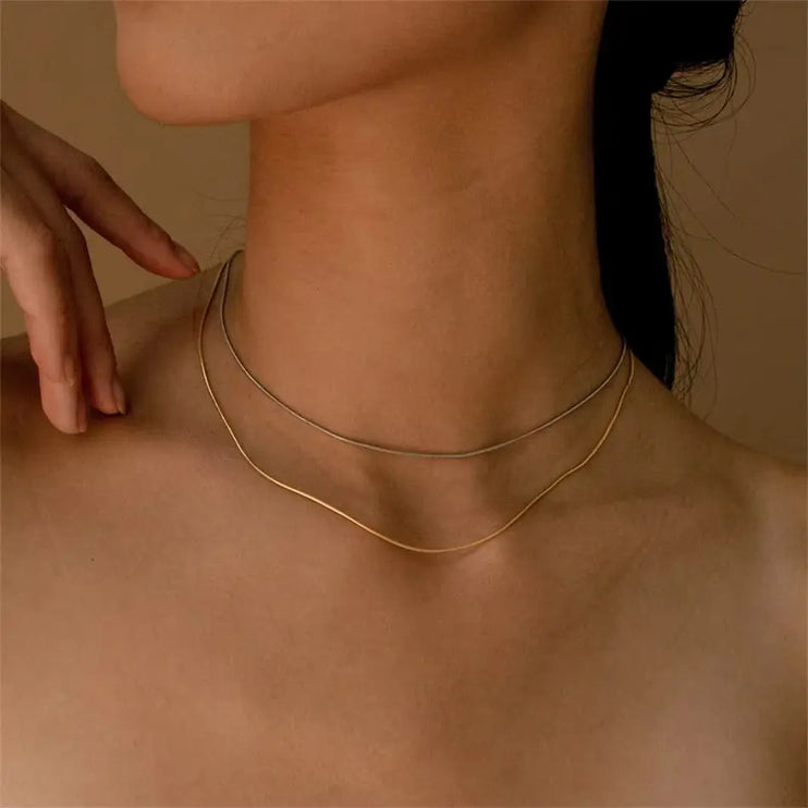 Gold necklace on a person's neck with a neutral background
