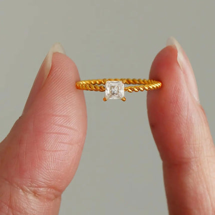 Gold ring with a diamond held between two fingers against a neutral background
