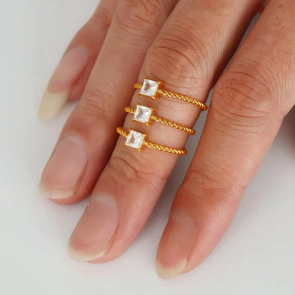 Hand wearing three gold rings with square gemstones on a white background
