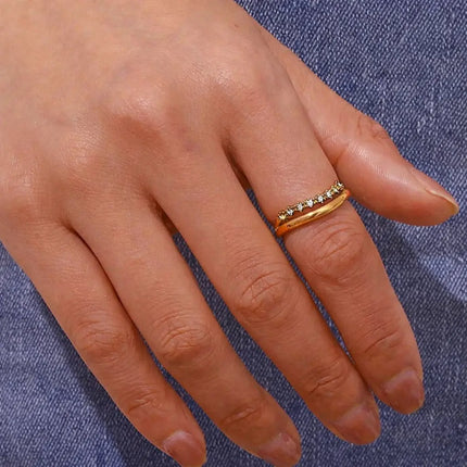 Close-up of a hand wearing a gold ring with gemstones on a blue denim background