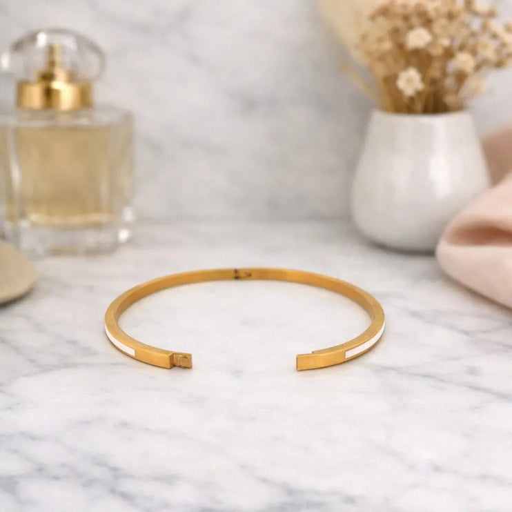 Gold bracelet on a marble surface with a perfume bottle and dried flowers in the background