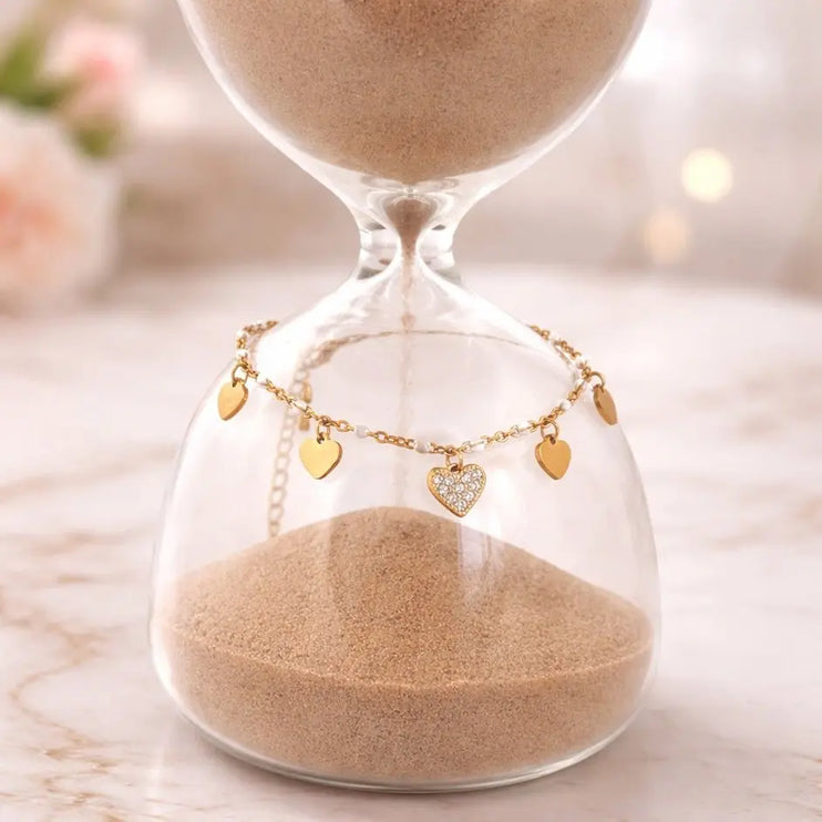 Hourglass with sand and a gold necklace with heart charms on a blurred background