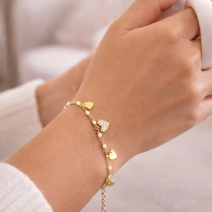 Gold bracelet with heart-shaped charms on a wrist against a neutral background