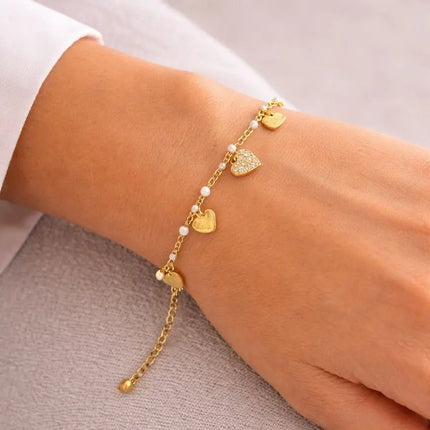 Gold bracelet with heart charms on a wrist against a neutral background