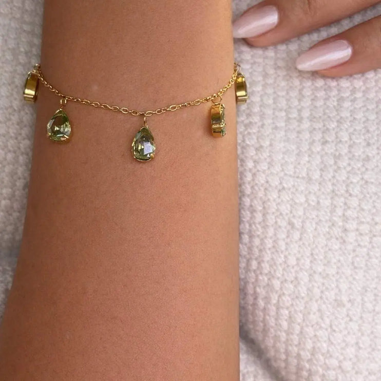 Gold bracelet with green gemstones on a wrist against a textured light background