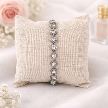 Silver bracelet on a textured pillow with floral and product in the background