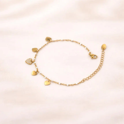 Gold bracelet with heart-shaped charms on a light pink background
