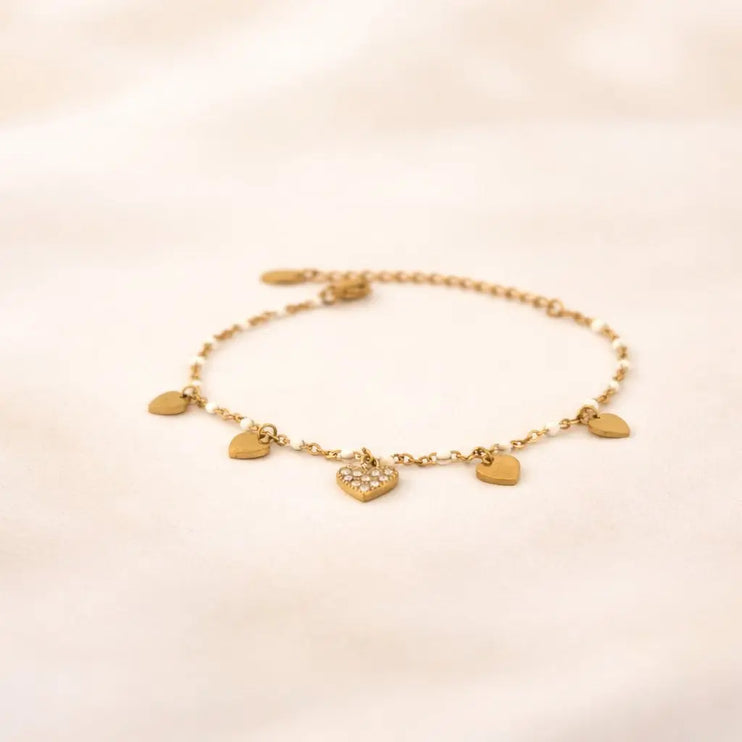 Gold bracelet with heart-shaped charms on a beige background