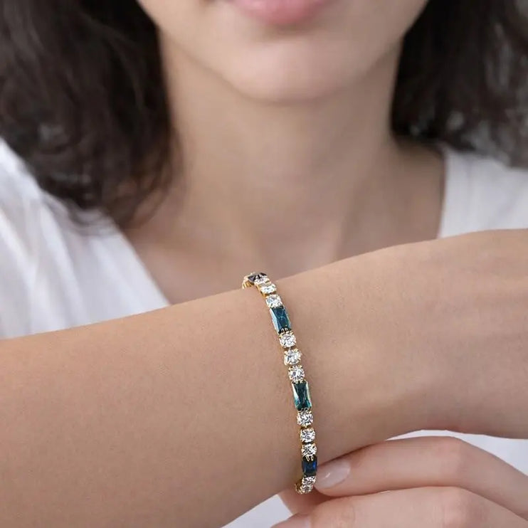 Close-up of a person wearing a bracelet with blue and clear stones on a plain background
