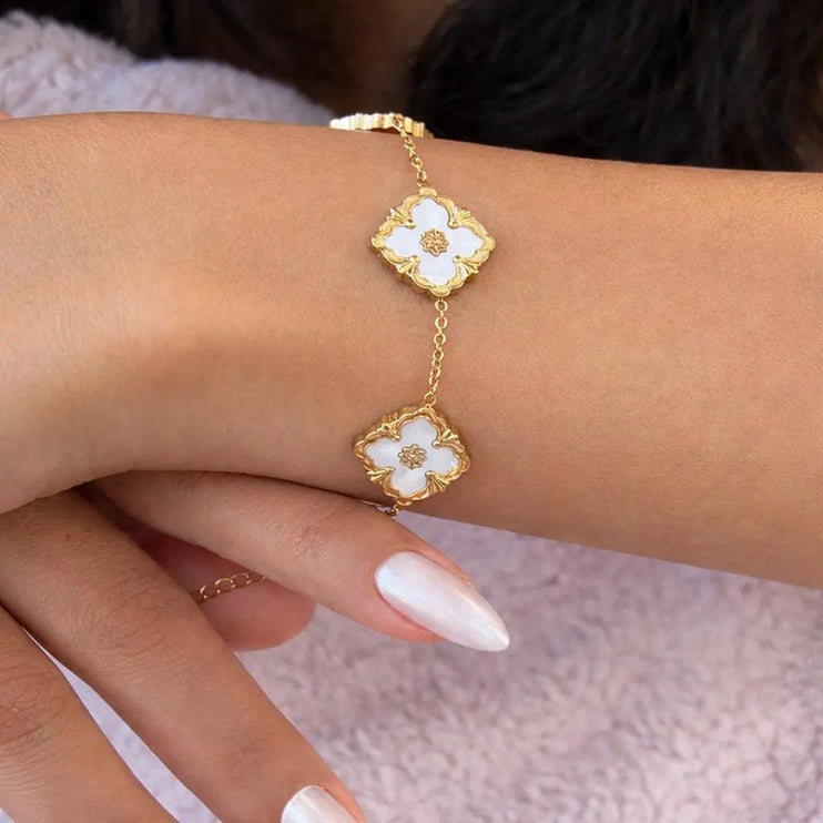 Gold bracelet with white flower designs on a wrist against a blurred background