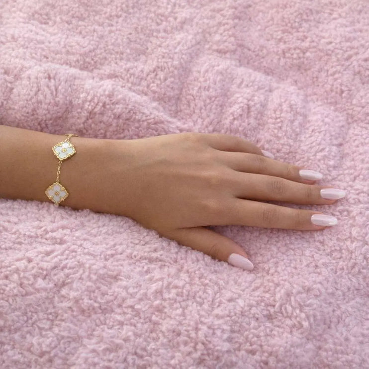 Hand wearing a gold bracelet on a pink textured surface