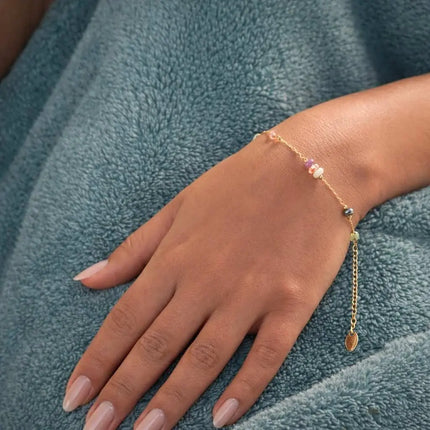 Hand wearing a gold bracelet with small beads on a textured blue fabric background