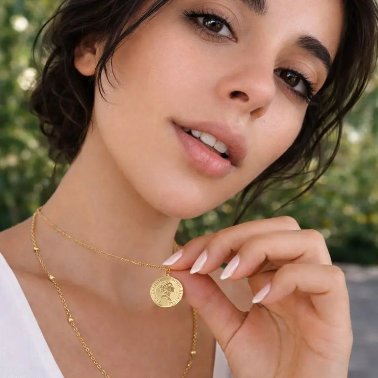 Woman wearing a gold necklace with a coin pendant, outdoors.