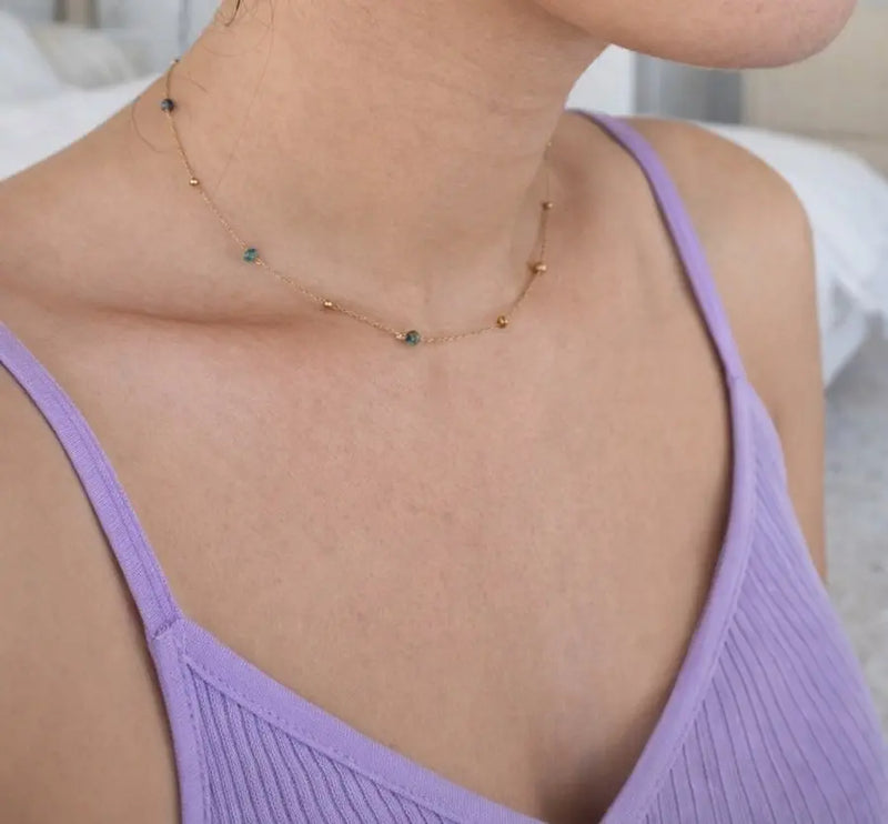 Necklace with small beads worn by a person in a purple top.