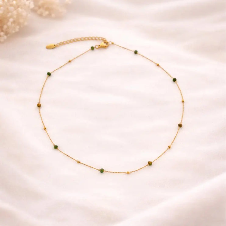 Delicate gold necklace with green beads on a soft beige background