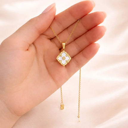 Gold necklace with a clover-shaped pendant held in a hand against a light background