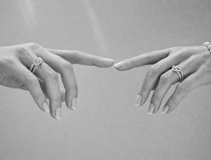 Two hands with rings pointing towards each other on a gray background