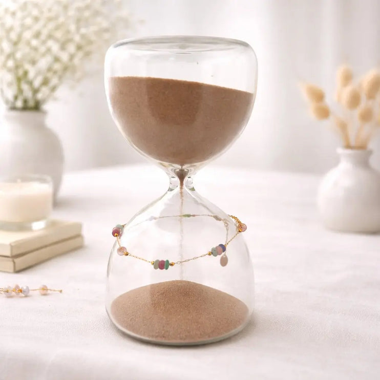 Glass hourglass with sand on a white surface with decorative items in the background
