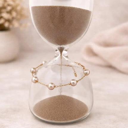 Glass hourglass with sand and a pearl bracelet on a neutral background