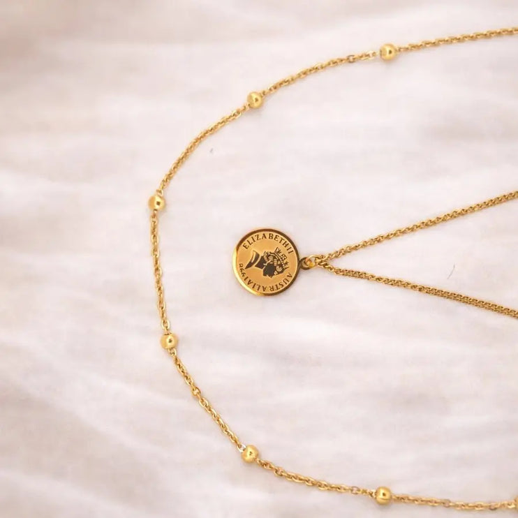 Gold necklace with a round pendant on a light pink background