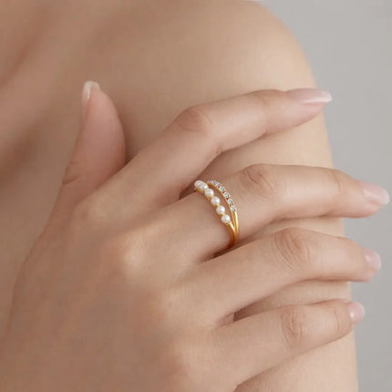 Hand wearing a gold ring with pearls on a neutral background