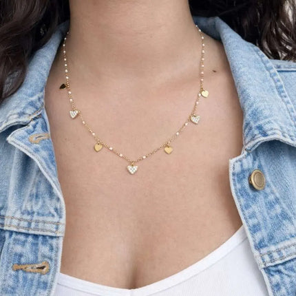 Person wearing a gold necklace with heart-shaped pendants, wearing a denim jacket.