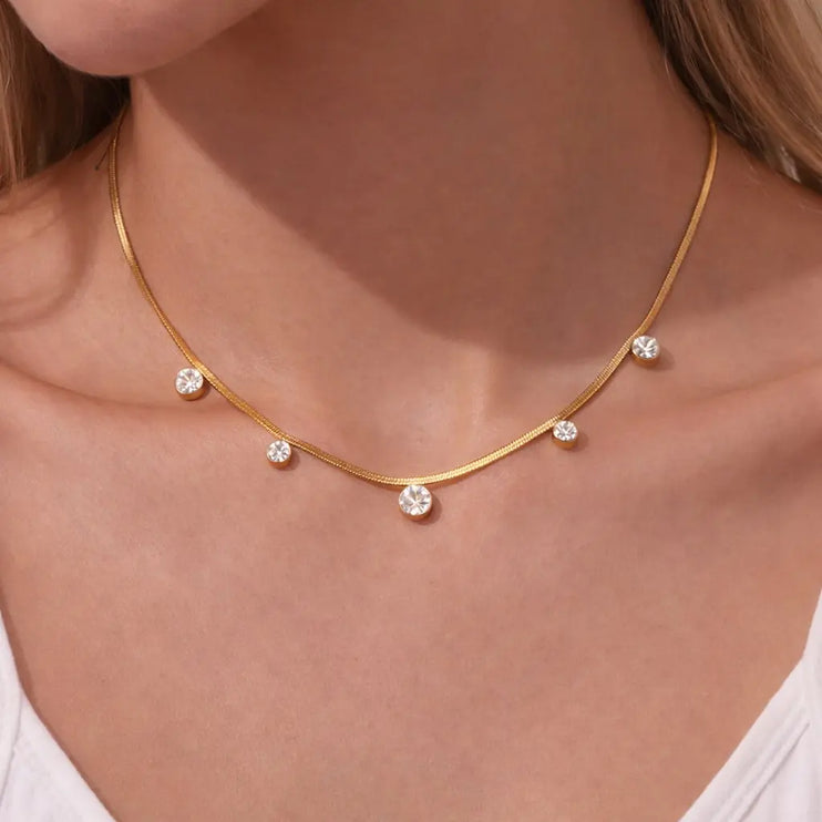 Gold necklace with small diamonds on a person wearing a white top