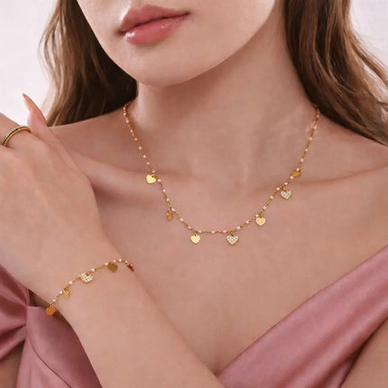 Close-up of a woman wearing a gold necklace and bracelet with heart-shaped charms.