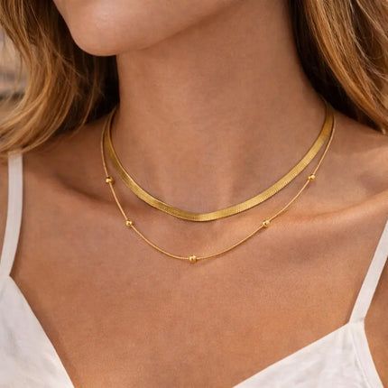 Minimalist gold stainless steel necklace worn by a woman, featuring layered chains with small bead accents