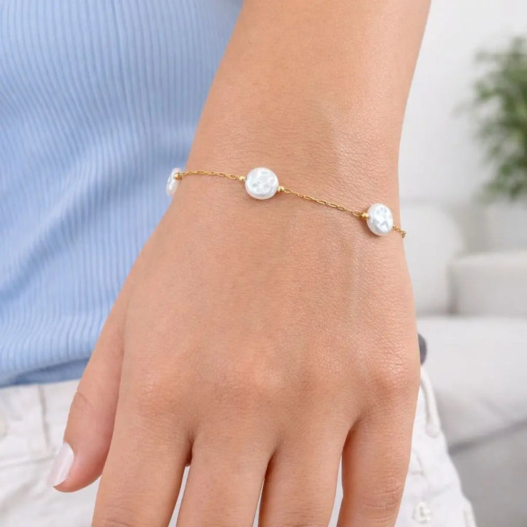 Gold bracelet with white beads on a wrist against a blurred background