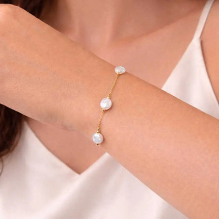 Gold bracelet with pearl beads on a wrist against a neutral background