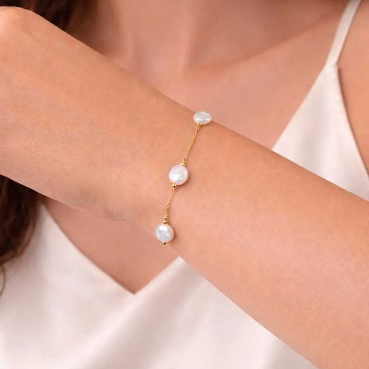 Gold bracelet with pearl beads on a wrist against a neutral background