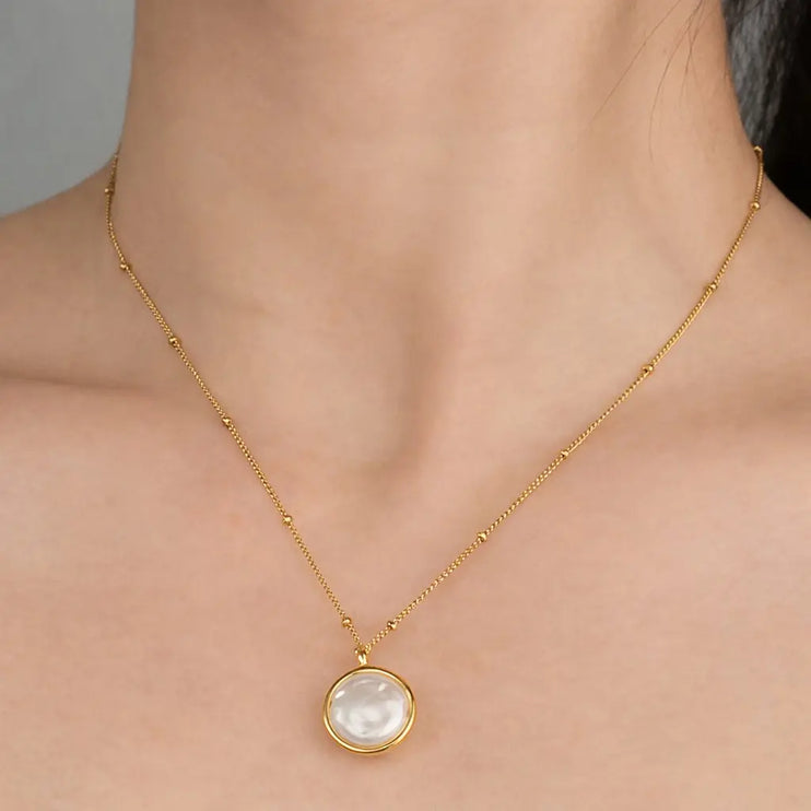 Gold necklace with a pendant on a person's neck against a neutral background