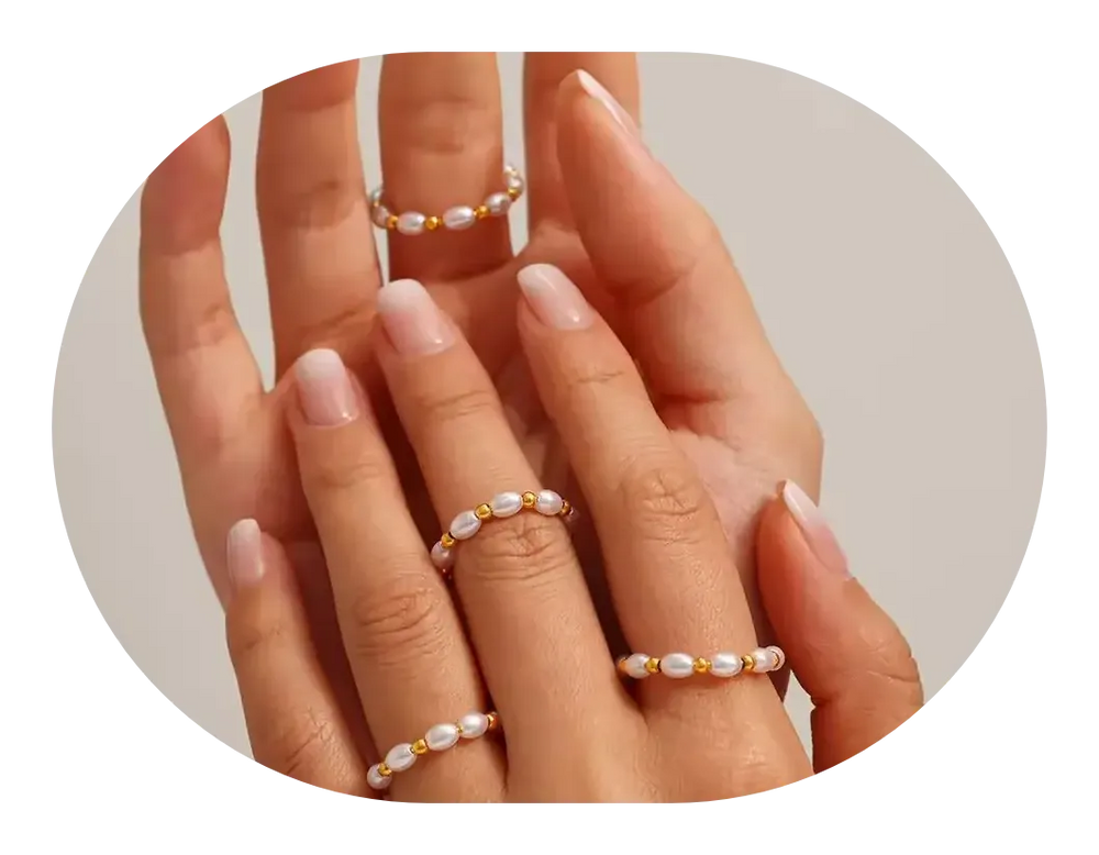 Hand wearing multiple pearl rings on a neutral background