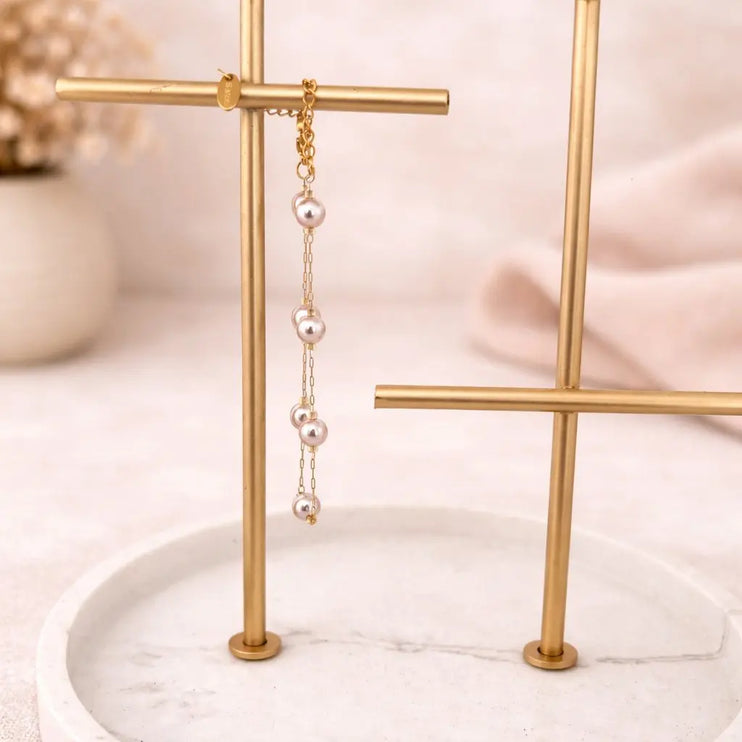 Pearl earring on a gold stand with a soft pink background