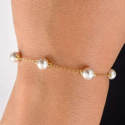 Gold bracelet with pearls on a wrist against a neutral background