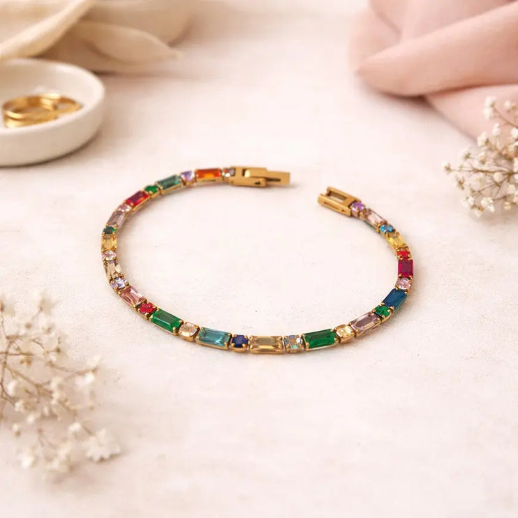 Multicolored gemstone bracelet on a light surface with a hand and small bowl in the background.