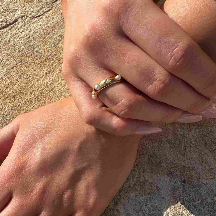 Close-up of a hand wearing a gold ring with pearls on a textured surface