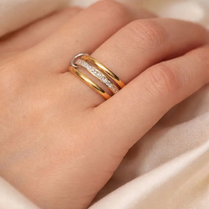 Close-up of a hand wearing two gold rings with diamond accents on a beige fabric background